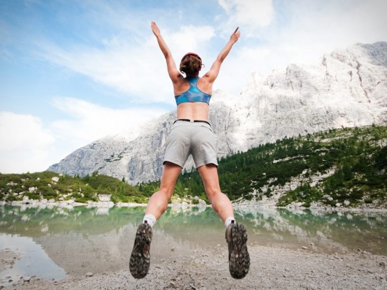 woman jumping wearing blue sports bra and grey shorts